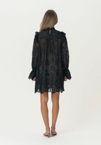 Schwarzes Spitzenkleid mit langen Ärmeln, Rüschendetails und einem Schlüsselloch-Ausschnitt hinten. Mit floralen Mustern und einem leicht ausgestellten Saum.