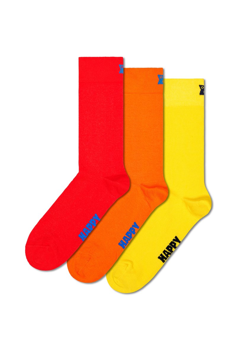 Zestaw trzech skarpetek: czerwone, pomarańczowe i żółte. Każda skarpetka ma prążkowany mankiet i niebieski napis "HAPPY" z boku. Gładka tekstura.