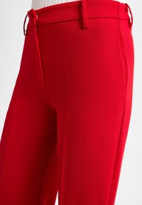 Rode op maat gemaakte broek van glad, lichtgewicht materiaal met een aansluitend ontwerp. Bevat zijzakken en een ritssluiting met riemlussen.