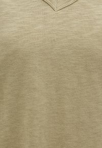 Beige V-neck pullover made of soft, textured knit fabric with a subtle heather pattern, featuring a stitched neckline and no visible hardware.