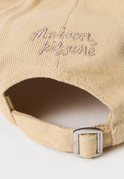 Beige szövet sapka hímzett "maison kitsuné" felirattal és állítható fém csattal, amelyen a márkanev is gravírozva van.