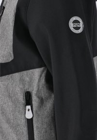 Zwarte en grijze jas met een gestructureerde stof, een ritszak en een cirkelvormige logo patch op de schouder.