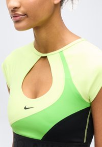 Γυναίκα που φοράει πράσινο και μαύρο αθλητικό τοπ Nike με άνοιγμα στο λαιμό και κοντά μανίκια, εμφανίζοντας τον λαιμό και το πάνω μέρος του στήθους.