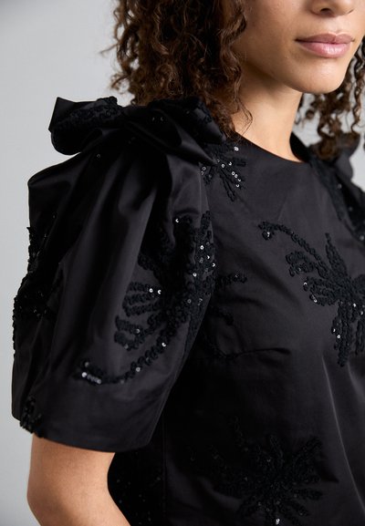 Top nero con collo rotondo, maniche a sbuffo e motivi floreali realizzati in paillettes e embellimenti in tessuto testurizzato.