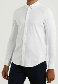 Biała, długosleeve koszula zapinana na guziki wykonana z lekkiego materiału, z klasycznym kołnierzykiem, subtelnym logo i zaokrąglonym dołem.