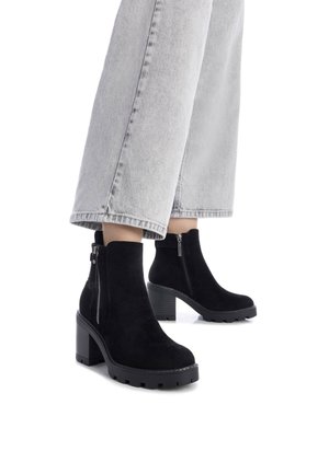 Stivali alla caviglia in suede nero con tacco a blocco e cerniera laterale, caratterizzati da una suola testurizzata e una parte superiore liscia, abbinati a jeans a gamba larga grigio chiaro.
