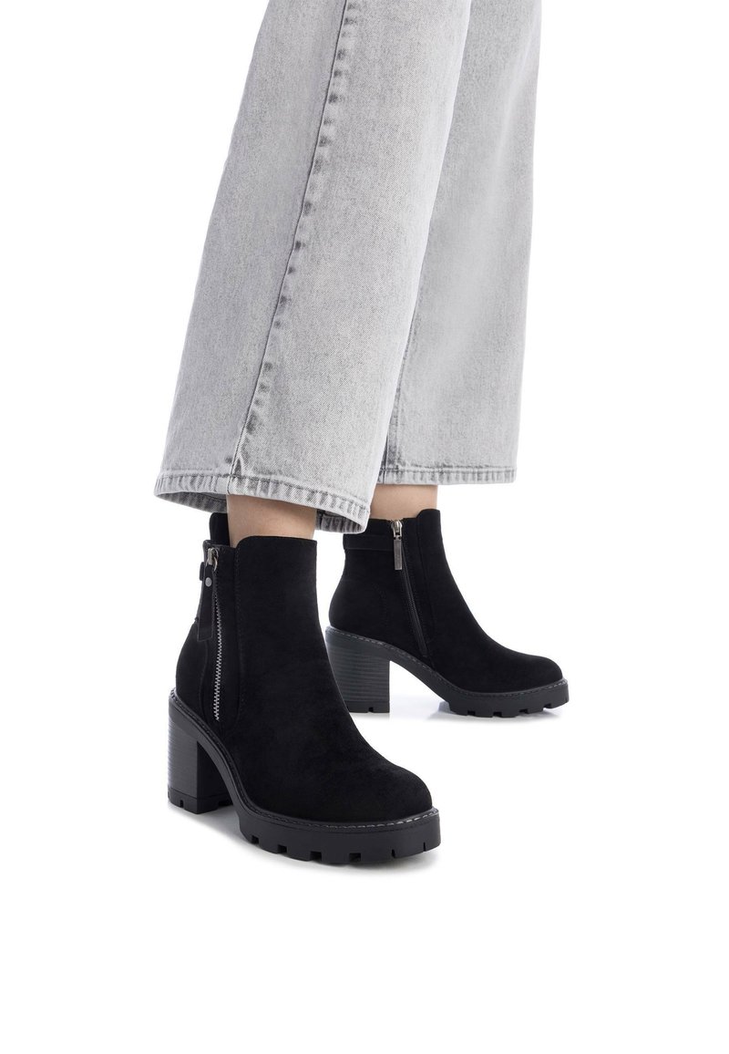Botas de ante negras hasta el tobillo con un tacón cuadrado y cremallera lateral, que presentan una suela texturizada y parte superior suave, combinadas con unos pantalones anchos de mezclilla gris claro.