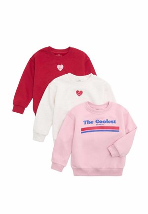 Trzy bluzy dziecięce w kolorach czerwonym, białym i różowym; czerwone i białe mają uśmiechnięte grafikę serca, różowa ma napis "The Coolest Being Me" z paskami.