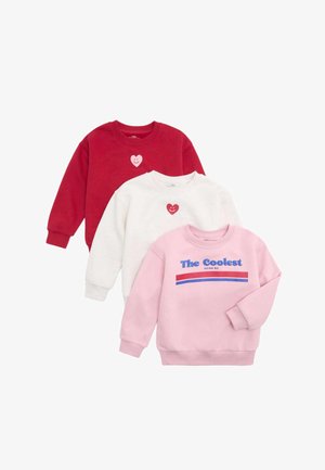 Trzy bluzy dziecięce w kolorach czerwonym, białym i różowym; czerwone i białe mają uśmiechnięte grafikę serca, różowa ma napis "The Coolest Being Me" z paskami.