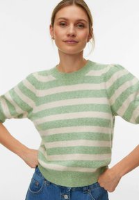 Pull rayé vert et crème à manches courtes, col et ourlet côtelés, fabriqué à partir d'un tissu doux et texturé. Porté avec un jean en denim bleu.