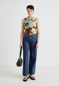 Top in tie-dye multicolore, jeans a vita alta blu a gamba larga, sandali neri con punta quadrata e una piccola borsa nera.