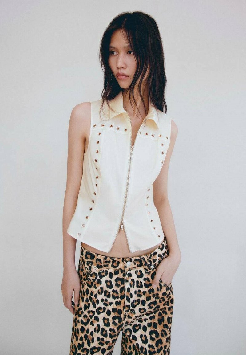 Cropped in pelle bianca con zip frontale e dettagli borchiati, abbinato a pantaloni a vita alta con stampa leopardata e chiusura a bottone.