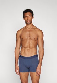 Dunkelblaue Boxershorts aus einem glatten, dehnbaren Stoff mit einem breiten, elastischen Bund, der ein dezentes Logo-Design aufweist.