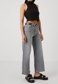 Svart ribbad kort topp, grå vida jeans med slitna detaljer, silvrig nitarbälte och svarta chunky sandaler.