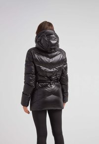 Czarna kurtka puchowa z wąską talią i dużym kapturem. Posiada błyszczącą, pikowaną teksturę oraz wzór w zygzak na plecach.