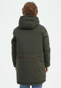 Parka rembourrée vert foncé avec capuche, dotée d'une poche zippée à l'arrière, d'un tissu texturé et d'une coupe droite qui arrive à mi-cuisse.