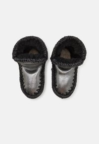 Zapatillas de cuero negro con un acabado metálico suave. Forro de felpa color crema, bordes cosidos y diseño de puño doblado.