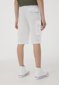 Pantaloni cargo bianchi in cotone con due tasche laterali, superficie testurizzata e orli risvoltati, abbinati a sneaker alte bianche.