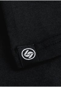 Black cotton fabric with fine ribbed texture, featuring a woven tag with a circular logo in white and black colors near the edge.
