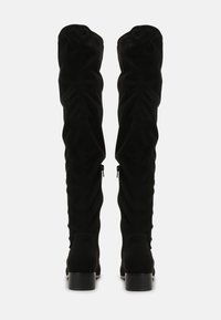 Black over-the-knee boots in soft suede with a ruched design. Features a round toe, block heel, and zipper details on the side.