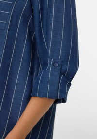 Blauwe gestreepte shirt met een gestructureerde stof, een knoopmanchet en contrasterende witte strepen, met een casual opgerolde mouwontwerp.