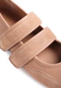 Κοντινό πλάνο ενός μπεζ παπουτσιού με δύο πλατιές λουρίδες σουέντ και δέρμα που στερεώνονται στο πάνω μέρος.
