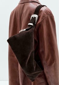 Brown suede shoulder bag with a triangular shape and smooth texture, featuring a silver metal buckle on a dark strap. The background is neutral.