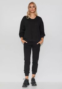 Czarna bluza i dopasowane dresy wykonane z miękkiego materiału. Bluza ma okrągły dekolt i luźny krój; dresy mają elastyczne mankiety.