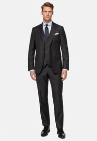 Completo giacca tre pezzi nero con rever a punta, tre bottoni e pantaloni abbinati. Completato con una camicia azzurra chiara e una cravatta scura. Scarpe eleganti.