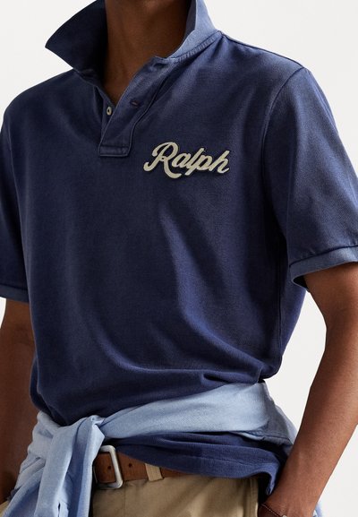 Jūras spēku stila polo krekls ar teksturētu apdari, ar salocītu apkakli un izšūtu "Ralph" logo krēmkrāsā. Gaiši zils džemperis, kas sasiets jostasvietā.