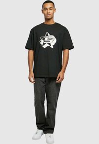 Sort t-shirt med et hvidt stjernesymbol og logo grafik, parret med mørkegrå jeans og hvide sneakers. Casual pasform med korte ærmer.