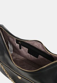 Bolso de mano de piel negra con cremallera dorada y cadena, abierto para mostrar el forro interior de tela beige con el logo de la marca y un bolsillo interior con cremallera.