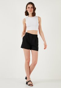 Fekete vászon rövidnadrág, magas derékkal, redőkkel és gombos záródással, fehér, testhezálló crop top-pal párosítva. Minimalista dizájn és sima textúra.