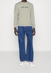 Felpa grigia con il testo "slow down" in verde, abbinata a jeans larghi blu e sneakers bianche con dettagli in rete e accenti viola.