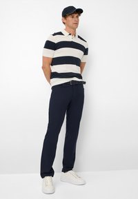 Polo avec des rayures horizontales bleu marine et crème, à manches courtes. Associé à un pantalon bleu marine et des baskets blanches, avec une casquette assortie en bleu marine.