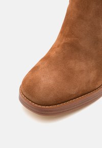 Ruske nubuk ankle boot z zaobljenim nosom in lesenim peto. Ima gladko teksturo in urejen stik z robom okoli podplata.