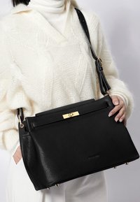 Sort lædertaske med tekstureret finish, gyldent hardware og en forlommer. Har en aftagelig rem og metalfødder.