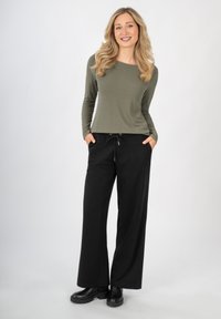 Top lungo verde oliva con un motivo testurizzato, abbinato a pantaloni neri a gamba larga con vita elastica e tasche laterali. Stivali neri.