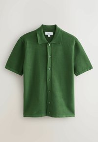 Polo à manches courtes tricoté vert avec des rayures horizontales texturées et une fermeture à boutons, posé à plat sur un fond clair.