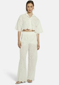 Witte eyelet crop top met gekartelde randen, gecombineerd met luchtige brede broek. Beide hebben geperforeerde patronen en een elastische tailleband.