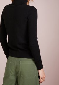 Czarny sweter z kołnierzem w miękkim dzianinowym materiale, dopasowany fason z długimi rękawami, połączony z oliwkowymi spodniami typu cargo o wysokim stanie.