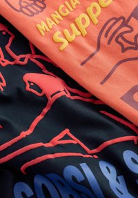 Nærbillede af stof med orange tekst "MANGIA supp" og håndillustrationer på koralfarvet baggrund, samt rødt lineart af fugle på sort baggrund.