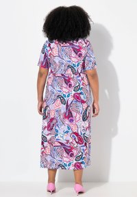 Vestido maxi con un vibrante patrón de paisley floral, que presenta mangas cortas, una cintura ajustada y una silueta fluida. Complementado con tacones rosas.