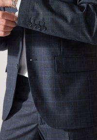 Giacca da uomo blu scuro con un motivo a quadri sottile, dotata di quattro bottoni neri sui polsini e di una tasca laterale diritta.