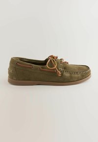 Mocassin en daim vert olive avec des lacets en cuir marron noués en nœud et semelle en caoutchouc, présenté de profil sur fond clair.