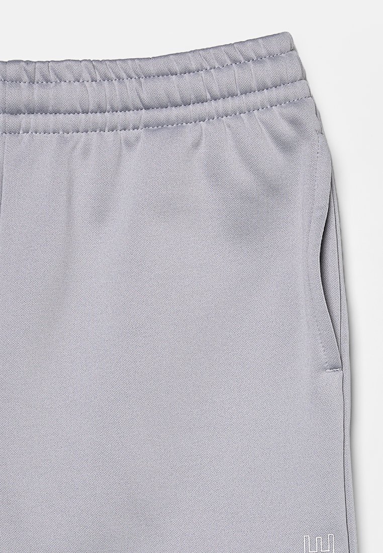 Pantalons de sport gris clair en matériau texturé, dotés d'une taille élastique et de poches latérales. Comprend un petit détail de logo.