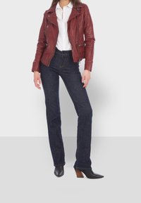 Rote Lederbikerjacke, weißes Hemd mit Knöpfen, dunkelblaue Denim-Jeans und schwarze spitze High Heels mit Holzabsatz.