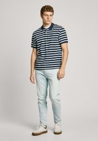 Navy and white striped polo shirt with a collar, paired with light blue denim jeans and white sneakers with dark accents.