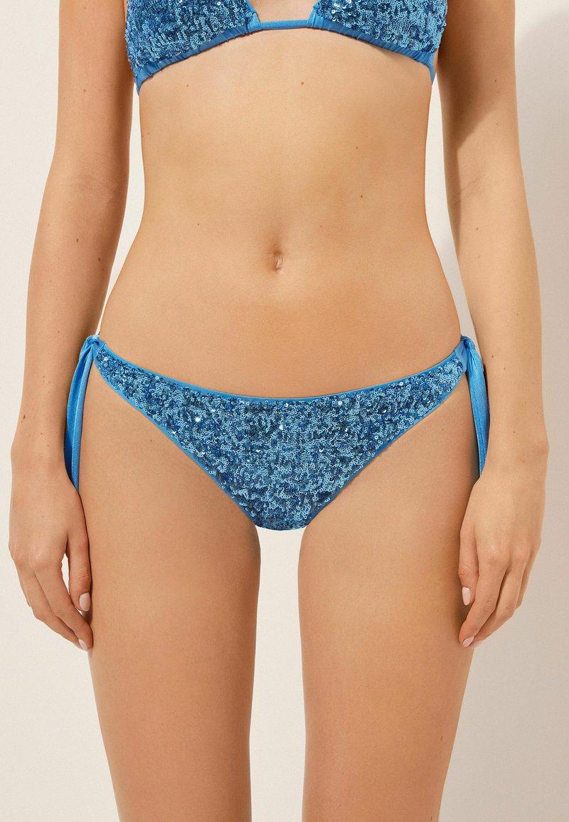 Blå bikiniunderdel med paljettmaterial, knytband på sidorna och en slät yta. Designen har en låg midja.