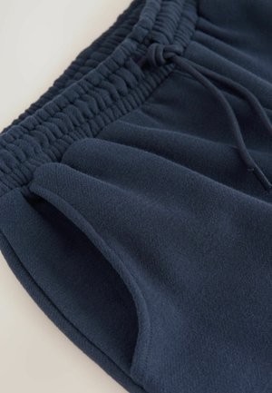 Tummansininen fleece-shortsit, joissa on gathered-vyötärö, nauhat yksityiskohtana ja sivutaskut; pehmeä rakenne ja siisti, minimalistinen muotoilu.